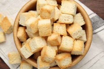 Delicious crispy croutons in bowl on wooden table, top view