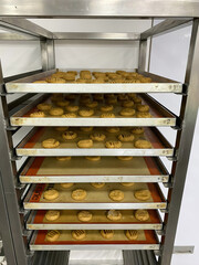 Racks hold trays of freshly baked cookies, arranged neatly in a lively bakery kitchen during the morning rush