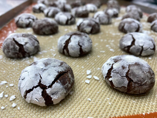 Chocolate crinkle cookies with powdered sugar cooling on a tray, showcasing their cracked and textured surface in a warm kitchen