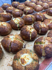 Freshly baked rolls with a golden crust and melted cheese are cooling in a lively bakery kitchen, filling the air with a delightful aroma