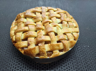 A freshly baked lattice pie sits on a textured surface, highlighting its golden-brown crust and inviting aroma