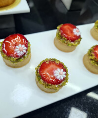 Freshly made pastry cups filled with cream, topped with strawberries, pistachios, and decorative flowers on a serving tray
