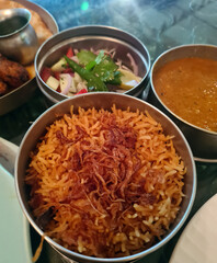 A delicious serving of biryani is presented in a metal container alongside fresh salad and rich curry, perfect for sharing at a family gathering