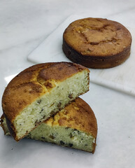 A delicious cake sits alongside slices on a cutting board, showcasing its moist texture and inviting aroma in a warm bakery atmosphere