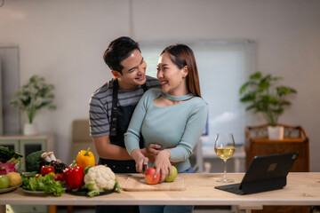 A man and a woman are standing in a kitchen, cutting vegetables