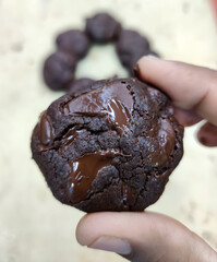 A hand holds a round piece of chocolate cookie dough above a tray lined with multiple cookie mounds, each waiting to be baked. The kitchen exudes a warm, inviting baking atmosphere