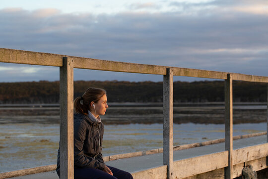 Teenager listening to music through earbuds on jetty at sunrise