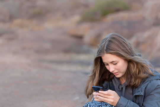 Teenager sitting outdoors at twilight and texting on smartphone - Powered by Adobe