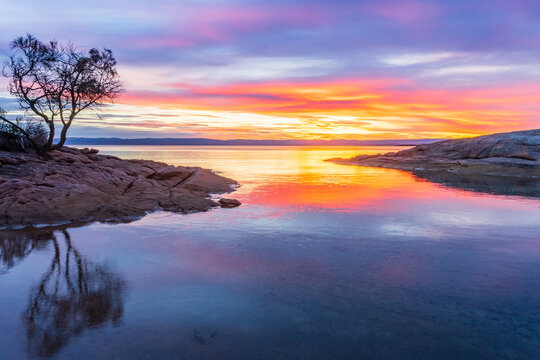 A vibrant sunset reflected in still water between two rocky points
