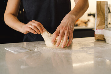 Hands are skillfully rolling and shaping dough on a clean kitchen countertop sprinkled with flour, healthy sourdough bread. The bright space suggests a cozy baking atmosphere.