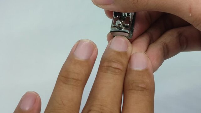 Cutting the nail of the middle finger of the left hand using a nail clipper on a white background