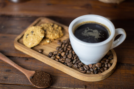 Hot black coffee white cup served with roasted beans, wooden coaster, cookies and tablespoon coffee powder on wooden background. hot black coffee for break time concept. Hot coffee in a cup. top view