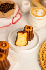 Canele cake - traditional French sweet dessert with the side part exposed served with white plate, three of canele on the side, beans jute sack, a cup of cappuccino coffee. article and recipe concept