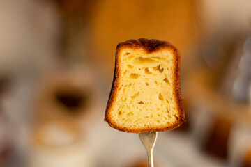 canele bread cut in half with a small gold fork with blurred background of dining table with canele...