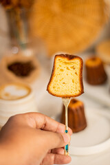 canele bread cut in half with a small gold fork with blurred background of dining table with canele on white plate, rattan tray and hot coffee cappuccino. canele of Bordeaux cut half expose concept