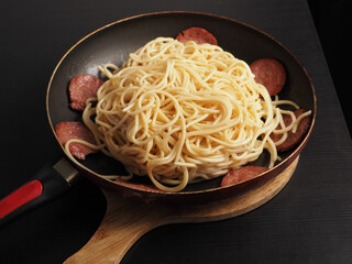 Spaghetti served in a frying pan with slices of sausage around the noodles ready for a tasty meal.
