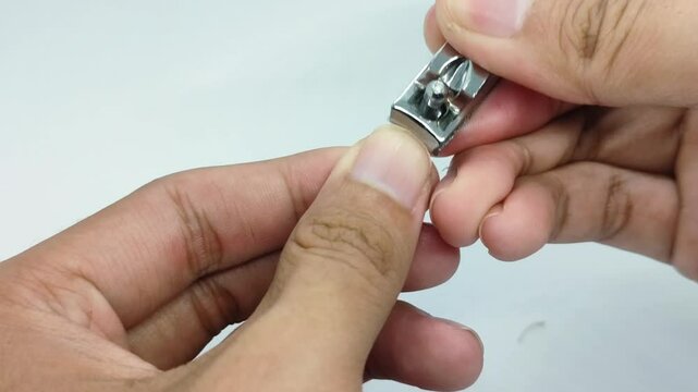 Cutting the thumbnail of the left hand using a nail clipper on a white background