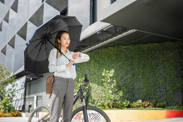 In the urban landscape a young woman with an umbrella rides her bicycle on a city street. She's a...