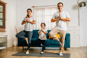 In their cozy living room Asian parents and their daughter engage in yoga and fitness exercises...