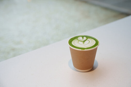 Paper cup filled with matcha latte, featuring intricate latte art in the shape of a heart. Enjoy beverage, Freshness and relaxation.