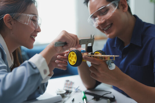 Asian engineers using caliper measuring robot prototype dimensions