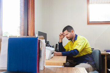 Male tradie at home office desk feeling overwhelmed and exhausted
