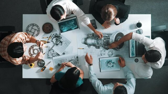 Top down aerial view of smart engineer team working together to design turbine engine. Professional technician discussing about jet engine construction while pointing at part of engine. Alimentation.