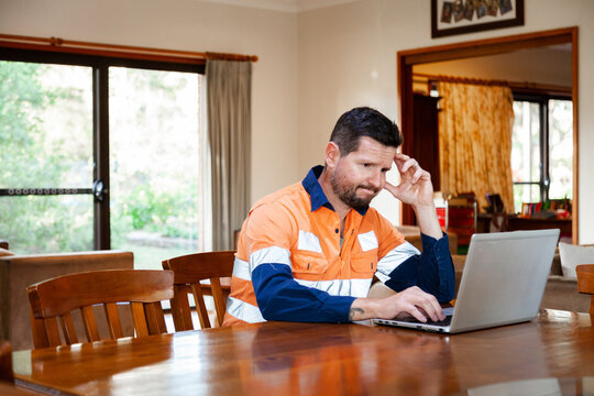 Male tradie in his 30s on laptop feeling overwhelmed and exhausted
