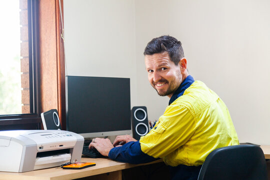 Happy male tradie at computer in home office