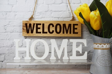 Welcome Home alphabet letters and wooden signboard hanging on white brick wall background