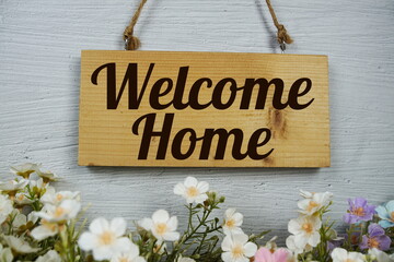Welcome Home text on wooden signboard hanging with flowers decoration on concrete background
