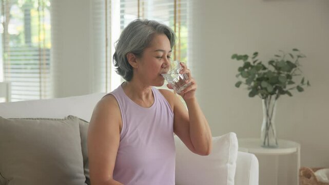 Asia adult aged people middle age happy old woman smile drink vitamin d c e k zinc omega 3 fish oil water pill reduce hot flash dry skin health care sit at home sofa elder aging asian. Take diet food.