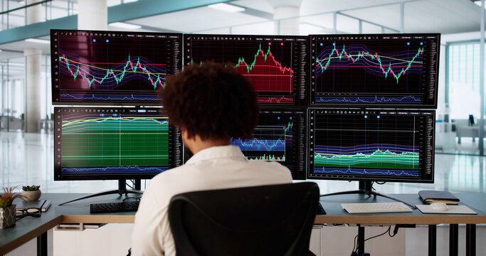 African American stock market broker analyzing graphs on multiple screens
