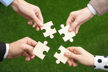 Teamwork. Group of people putting puzzle pieces together on blurred background, top view