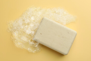 Soap bar with foam on yellow background, top view