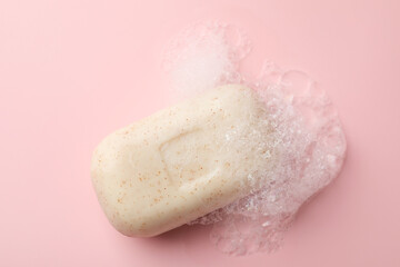 Soap bar with foam on light pink background, top view