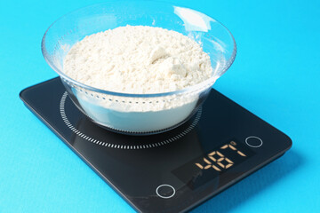 Electronic kitchen scale with flour on light blue background, closeup