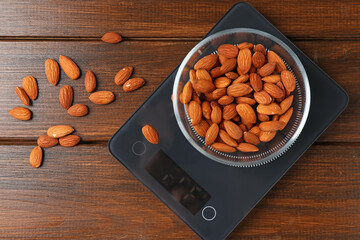 Electronic kitchen scale with bowl of almond nuts on wooden table, flat lay