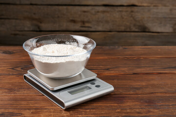Electronic kitchen scale with bowl of flour on wooden table. Space for text