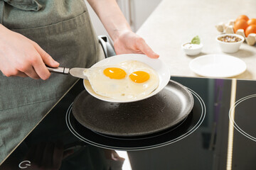 Woman putting tasty fried eggs onto plate in kitchen, closeup
