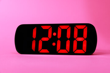 Digital alarm clock showing 12:08 o'clock on pink background, closeup
