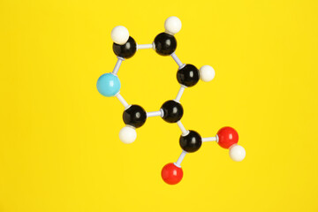 Molecule of niacin (vitamin B3) on yellow background. Chemical model