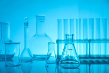 Laboratory glassware on mirror surface against light blue background