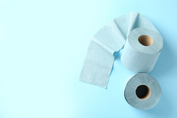 Color toilet paper rolls on light blue background, top view. Space for text