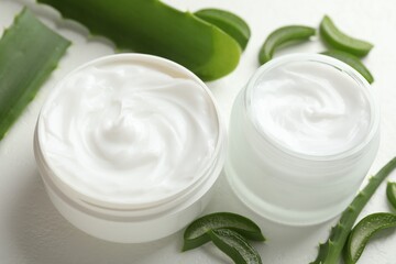 Moisturizing cream with extract of aloe vera and cut leaves on white textured background, closeup