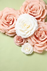 Beautiful paper flowers on light green background, flat lay. Space for text