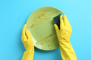Man washing dirty plate with sponge on light blue background, top view
