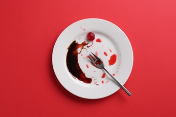 Dirty plate and fork on red background, top view