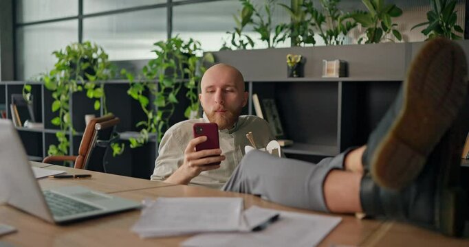 A humorous moment when a distracted office worker drops his phone while trying to eat lunch multitasking during a hectic workday in the office