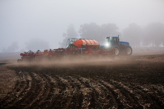 Fototapeta Horizontal shot of a blue tractor cultivating the soil in the field.